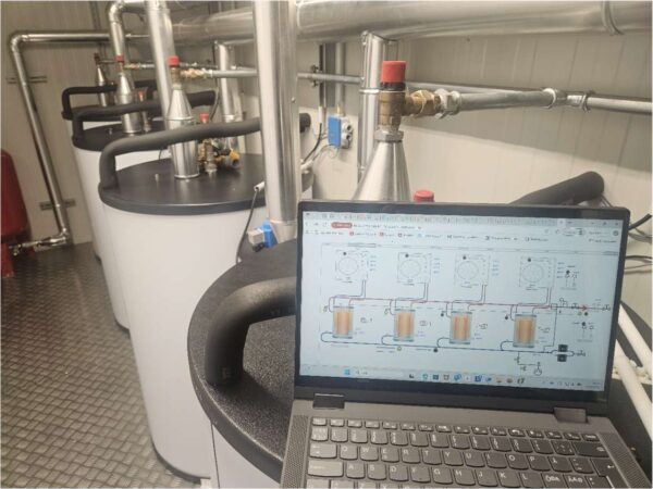 Tekniker med laptop ved buffertanker i energisentral